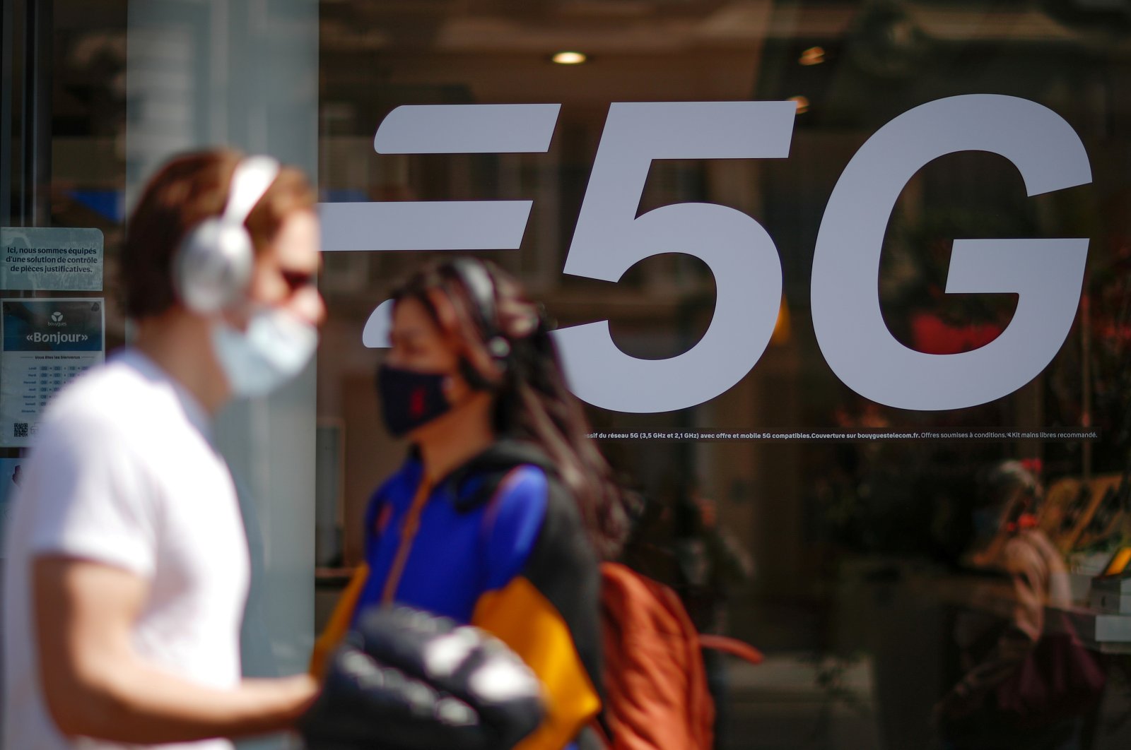 People wearing face masks walk past a 5G data network sign at a mobile phone store in Paris, France, April 22, 2021. (Reuters Photo)
