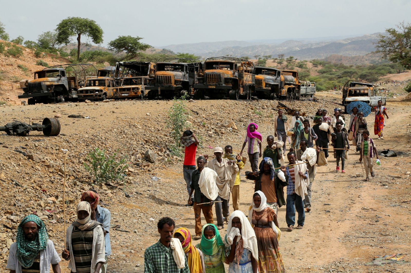 Villagers return from a market to Yechila town in south central Tigray walking past scores of burned vehicles, in Tigray, Ethiopia, July 10, 2021. (Reuters Photo)