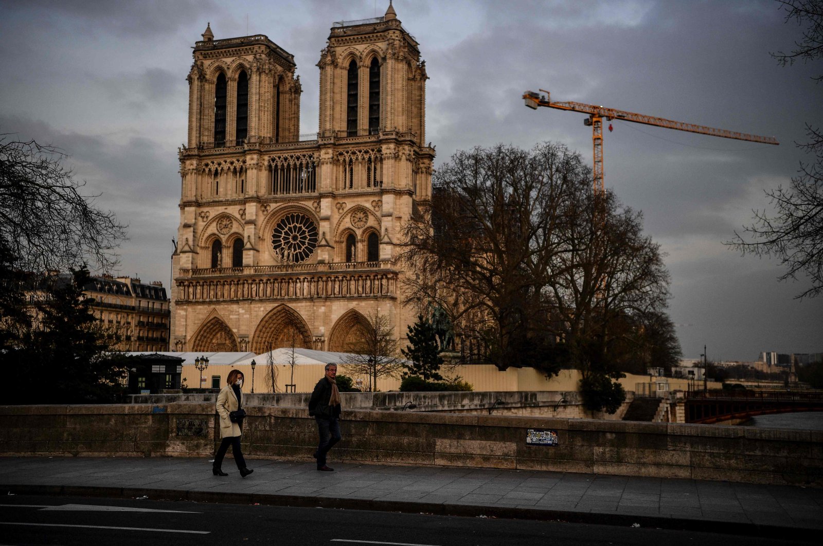 In this file photograph taken on March 17, 2020, a woman wearing a protective face mask and a man walk on a bridge over the Seine river near the Notre Dame de Paris cathedral in Paris. (AFP)