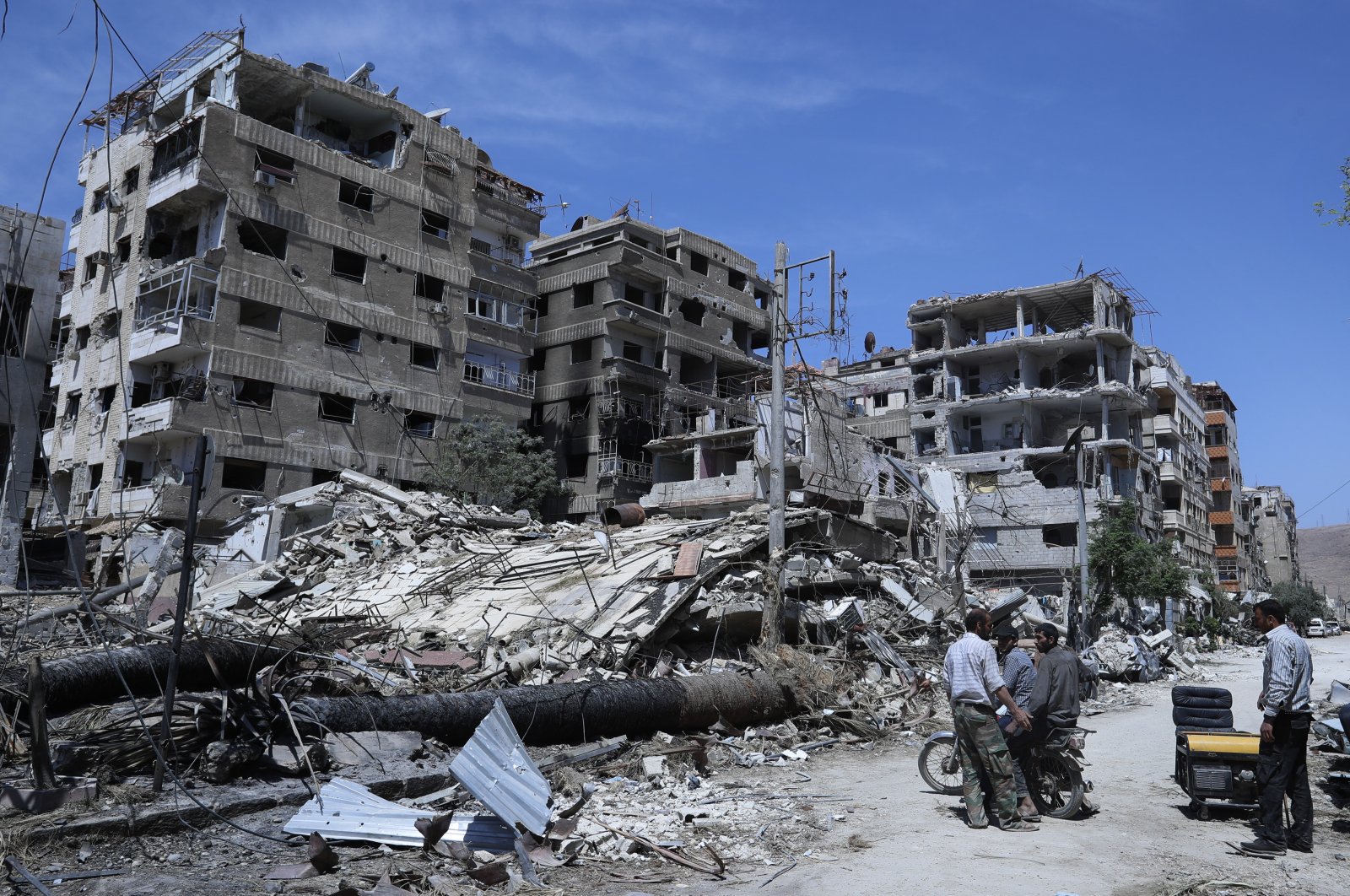 People stand in front of damaged buildings, in the town of Douma, the site of a suspected chemical weapons attack, near Damascus, Syria, April 16, 2018. (AP File Photo)