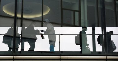 A member of staff wearing a protective suit checks the temperature of a passenger boarding an international flight at Narita International Airport on the first day of closed borders to prevent the spread of the new coronavirus omicron variant amid the coronavirus pandemic in Narita, east of Tokyo, Japan, Nov. 30, 2021. (Reuters Photo)