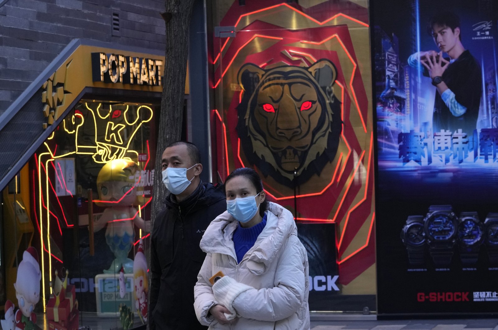 Residents wearing masks as protection against the coronavirus walk past shop decorations in Beijing, China, Nov. 30, 2021. (AP Photo)