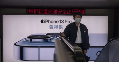 A man rides on the escalator in front of the advertisement for Apple’s iPhone 13 in Shanghai, China, Nov. 19, 2021. (EPA Photo)