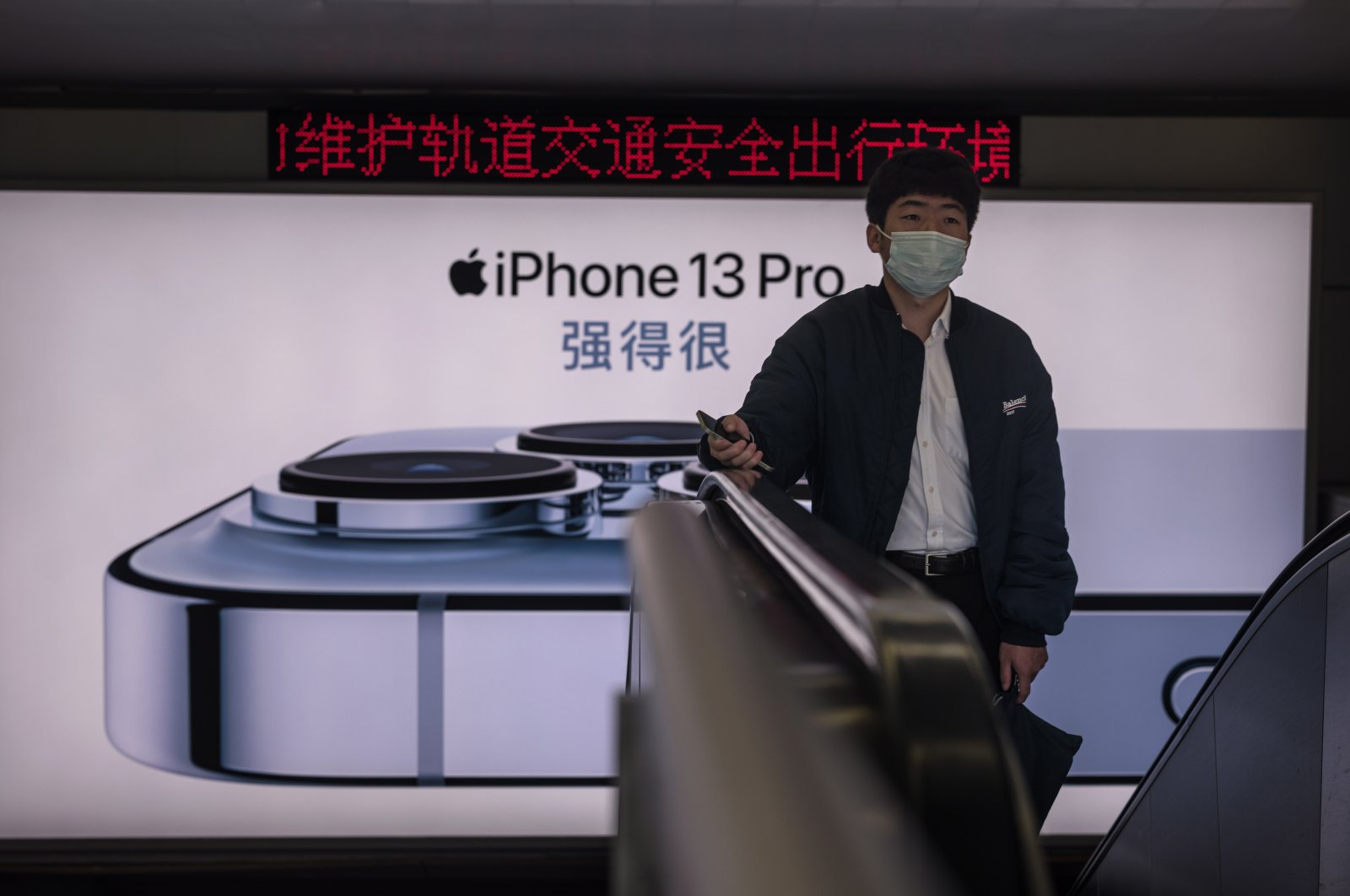 A man rides on the escalator in front of the advertisement for Apple’s iPhone 13 in Shanghai, China, Nov. 19, 2021. (EPA Photo)