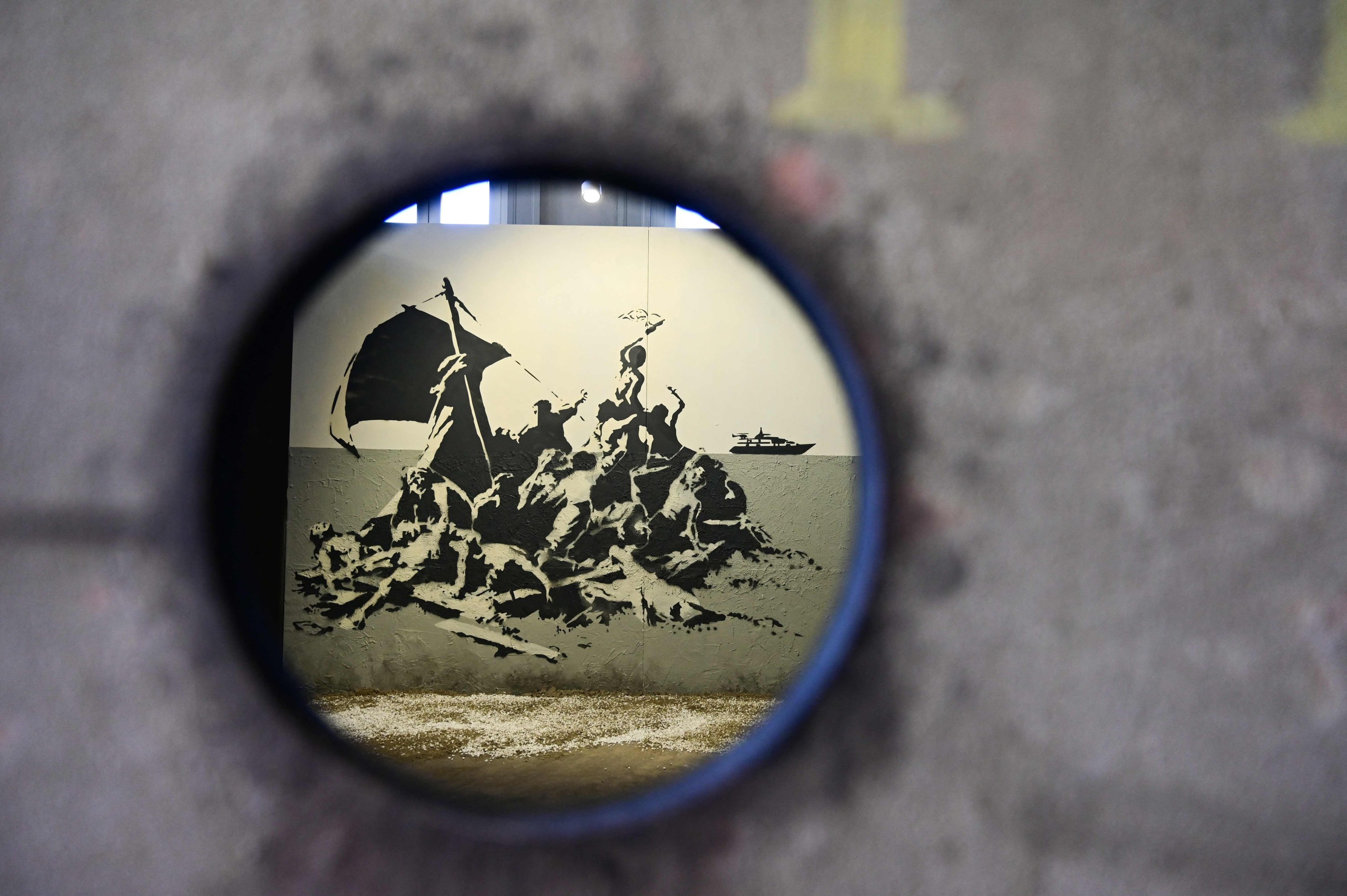 A picture taken through a hole shows British street artist Banksy's mural "Raft of the Medusa" during a preview of the exhibition “The Word of Banksy – The Immersive Experience" at the Milano Centrale main railway station in Milan, Italy on Dec. 2, 2021. (AFP)