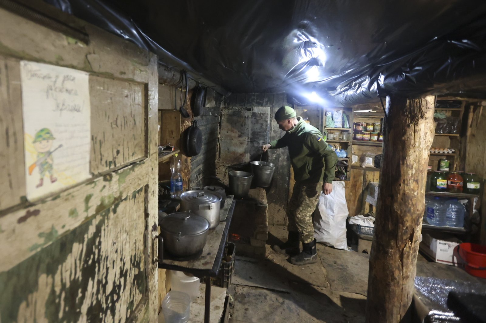A Ukrainian soldier cooks in a shelter near a fighting position on the line of separation from pro-Russian rebels near Debaltsevo, Donetsk region, Ukraine, Dec. 3, 2021. (AP Photo)