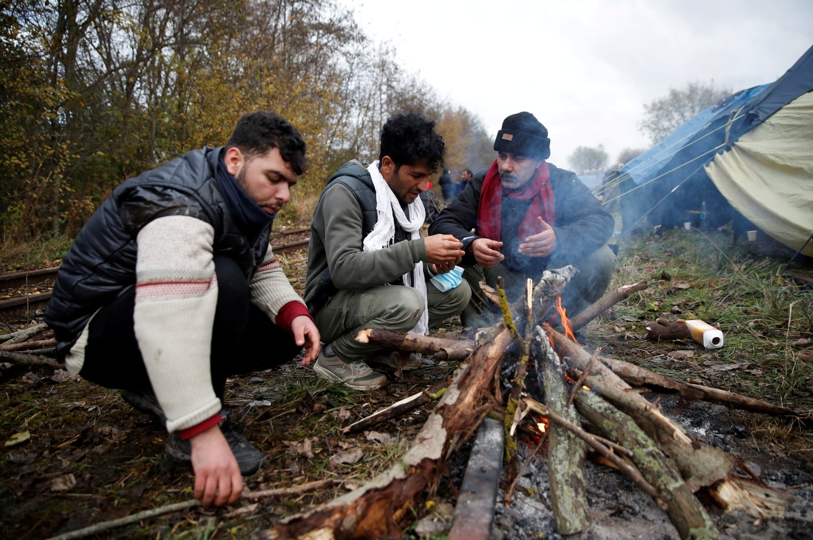 Migrants sit near a wood fire at a makeshift migrant camp in Loon Beach, the day after 31 migrants died when their dinghy deflated as they attempted to cross the English Channel, in Dunkirk, near Calais, France, Nov. 25, 2021. (Reuters Photo)