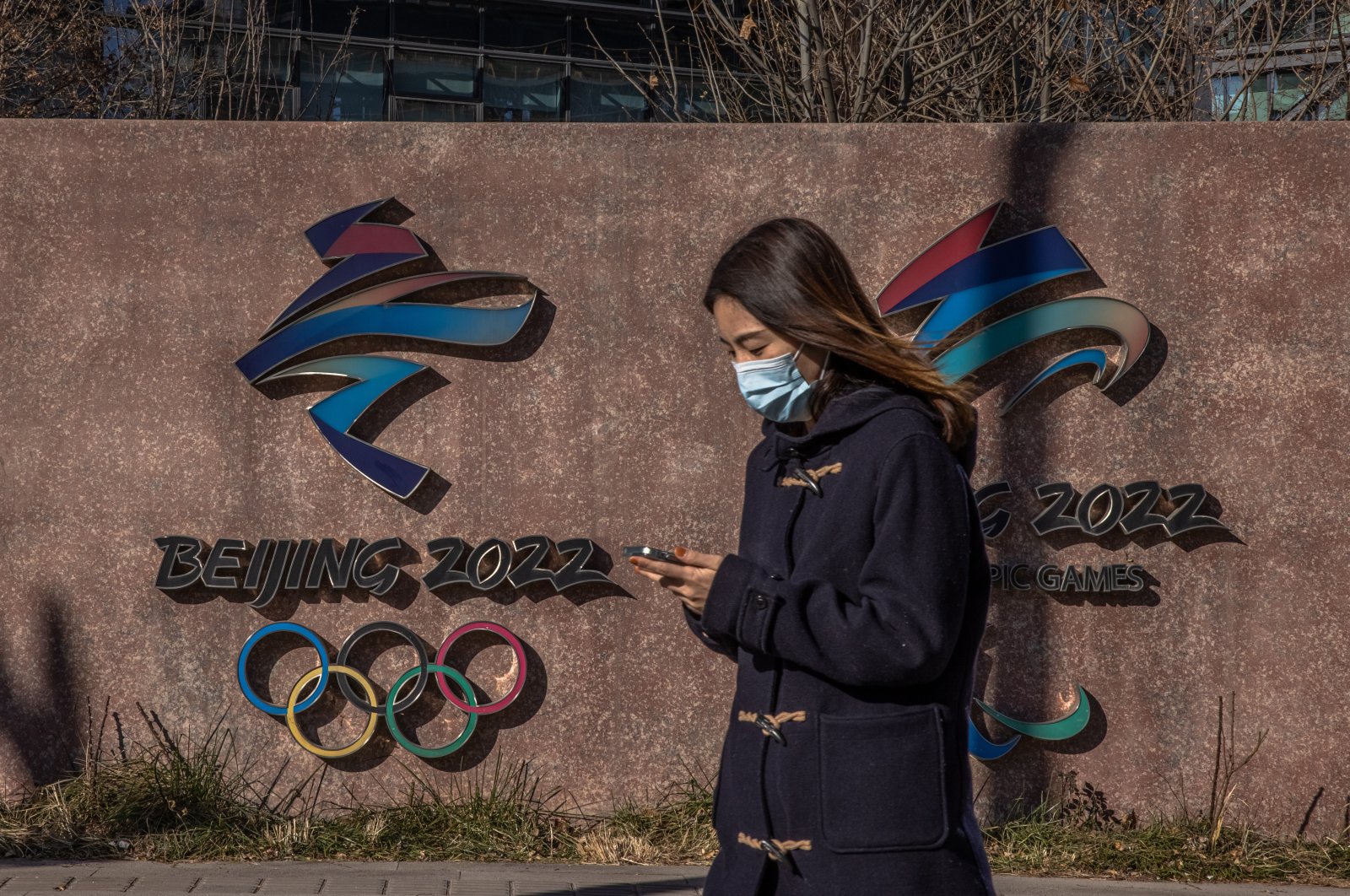 A woman wearing a face mask walks past the 2022 Beijing Winter Olympic and Paralympic emblems in Beijing, China, Dec. 1, 2021. (EPA Photo)