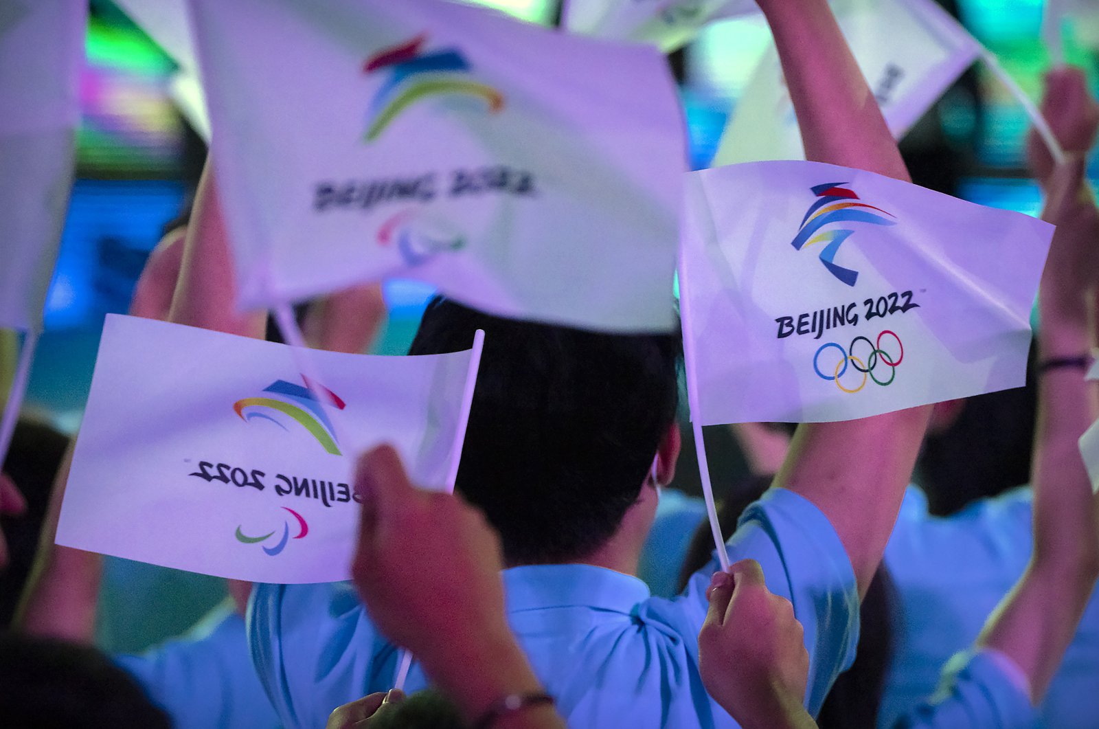 Participants wave flags with the logos of the 2022 Beijing Winter Olympics and Paralympics during an event in Beijing, China, Sept. 17, 2021. (AP Photo)