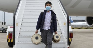 An Afghan boy carrying musical instruments disembarks from an airplane at a military airport, in Lisbon, Portugal, Dec. 13, 2021. (AP Photo)