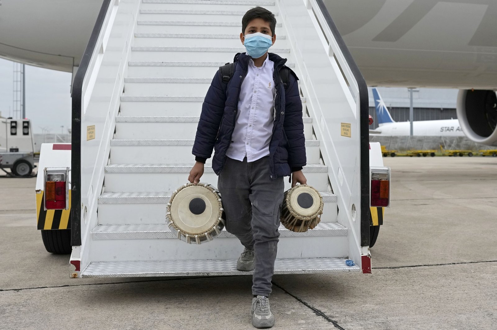 An Afghan boy carrying musical instruments disembarks from an airplane at a military airport, in Lisbon, Portugal, Dec. 13, 2021. (AP Photo)