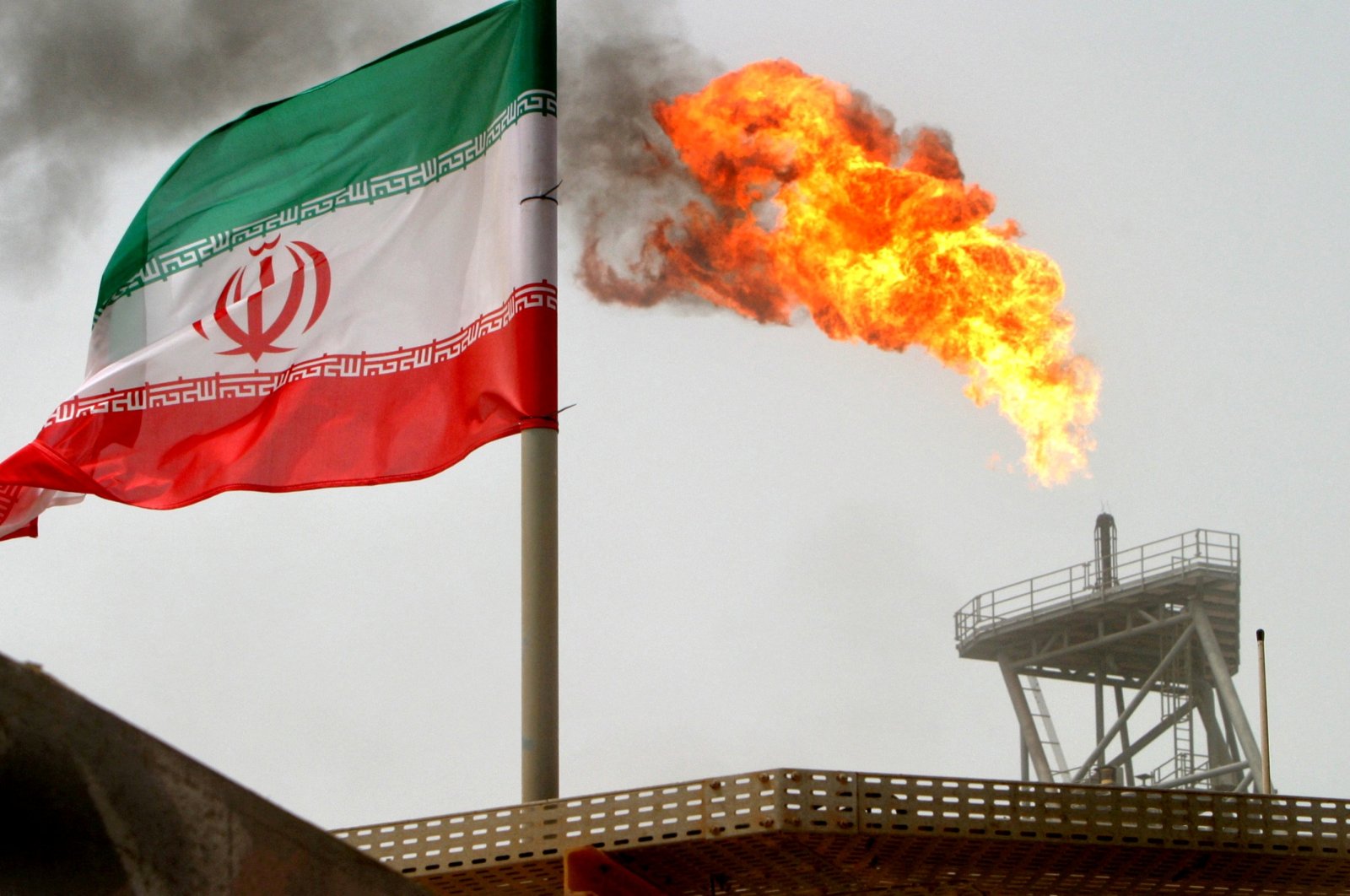 A gas flare-up on an oil production platform is seen alongside an Iranian flag in the Gulf, July 25, 2005. (Reuters Photo)