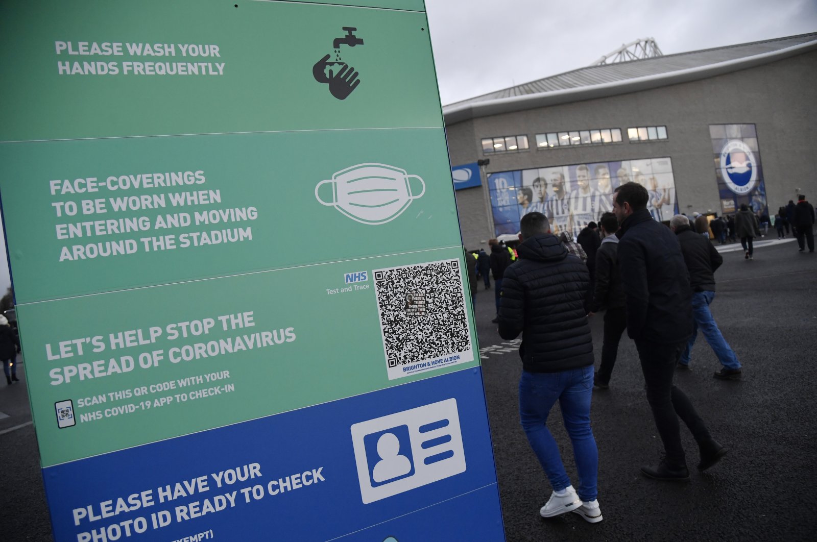 Football fans walk past a COVID-19 signage outside the American Express Community Stadium, Brighton, England, Nov. 27, 2021. (Reuters Photo)