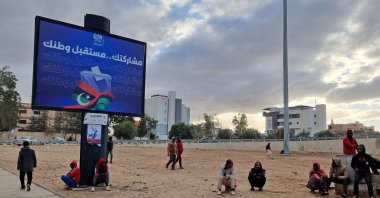Workers sit near an electoral billboard reading in Arabic "your participation is the future of your country" in Libya's capital Tripoli on Dec. 14, 2021. (AFP Photo)