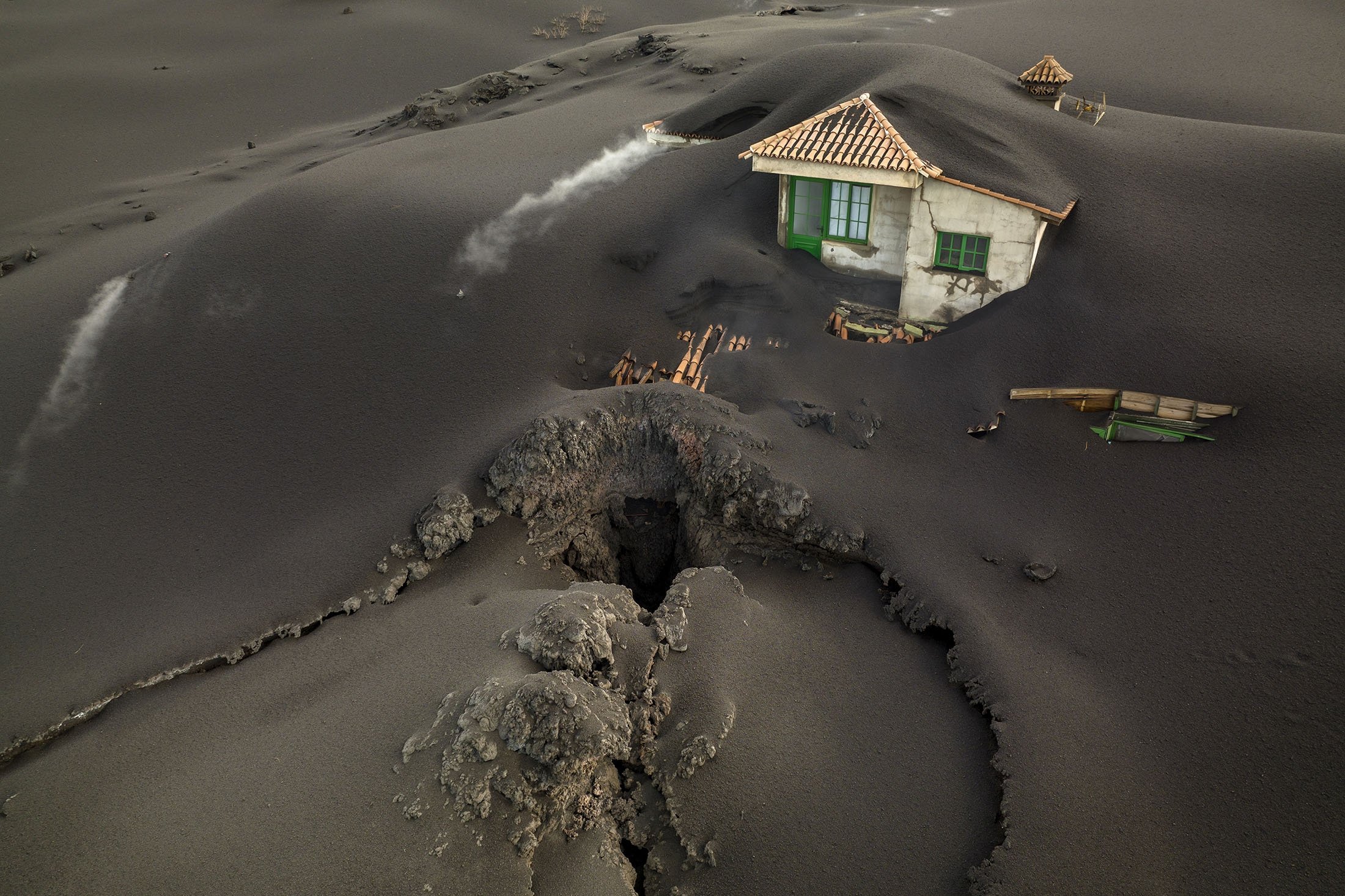 A fissure is seen next to a house covered with ash on the Canary island of La Palma, Spain, Dec. 1, 2021. (AP Photo)
