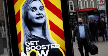 Pedestrians walk past a government advertisement promoting the NHS' COVID-19 vaccine booster program at a bus stop in London, U.K., Dec. 17, 2021. (AFP Photo)