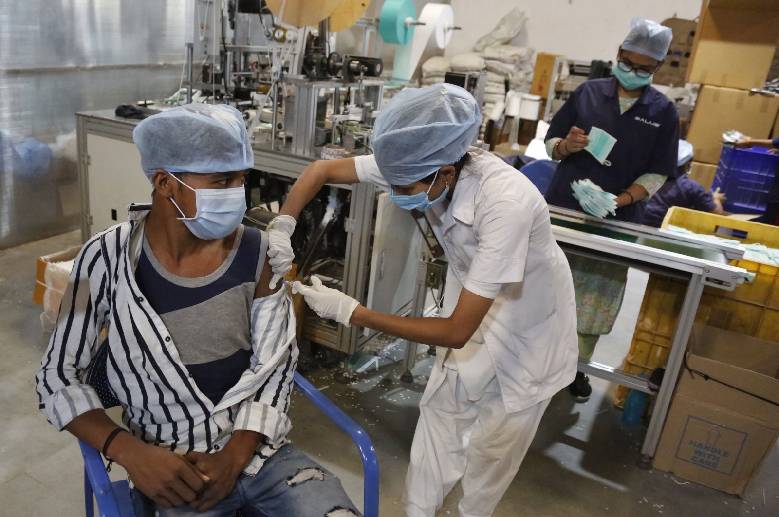 An Indian health worker administers the Covishield vaccine for COVID-19 to a worker at the factory of a face mask manufacturer on the outskirts of Ahmedabad, India, Friday, Dec. 17, 2021. (AP Photo)