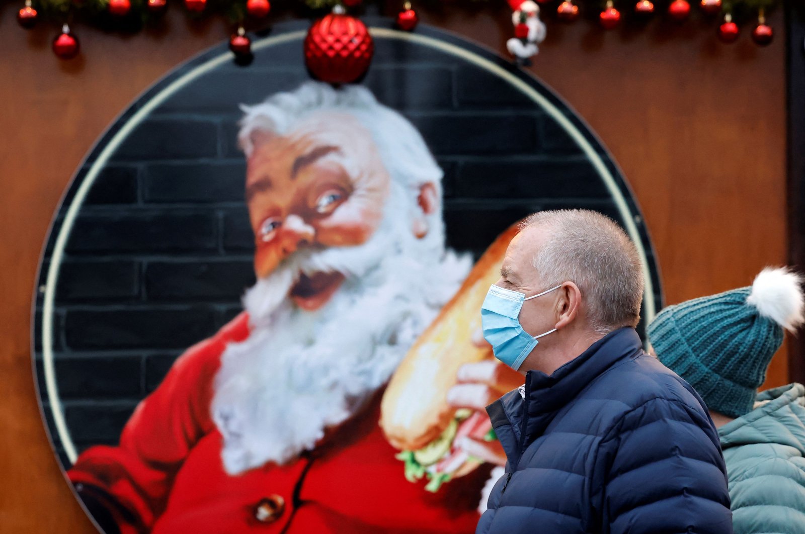 Shoppers, some wearing protective masks to combat the spread of Covid-19, walk past stalls at a Christmas market in central London, Britain, Dec. 18, 2021. (AFP Photo)