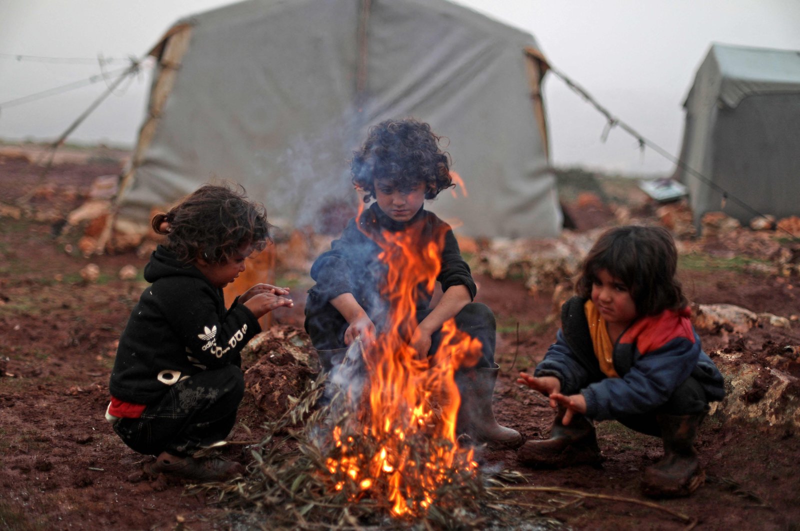 Children warm by the fire in a camp for displaced Syrians near the village of Kafr Uruq, in Syria&#039;s Idlib province, Dec. 17, 2021. (AFP Photo)