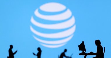 Small toy figures with laptops and smartphones are seen in front of displayed AT&T logo in this illustration, Dec. 5, 2021. (Reuters Photo)