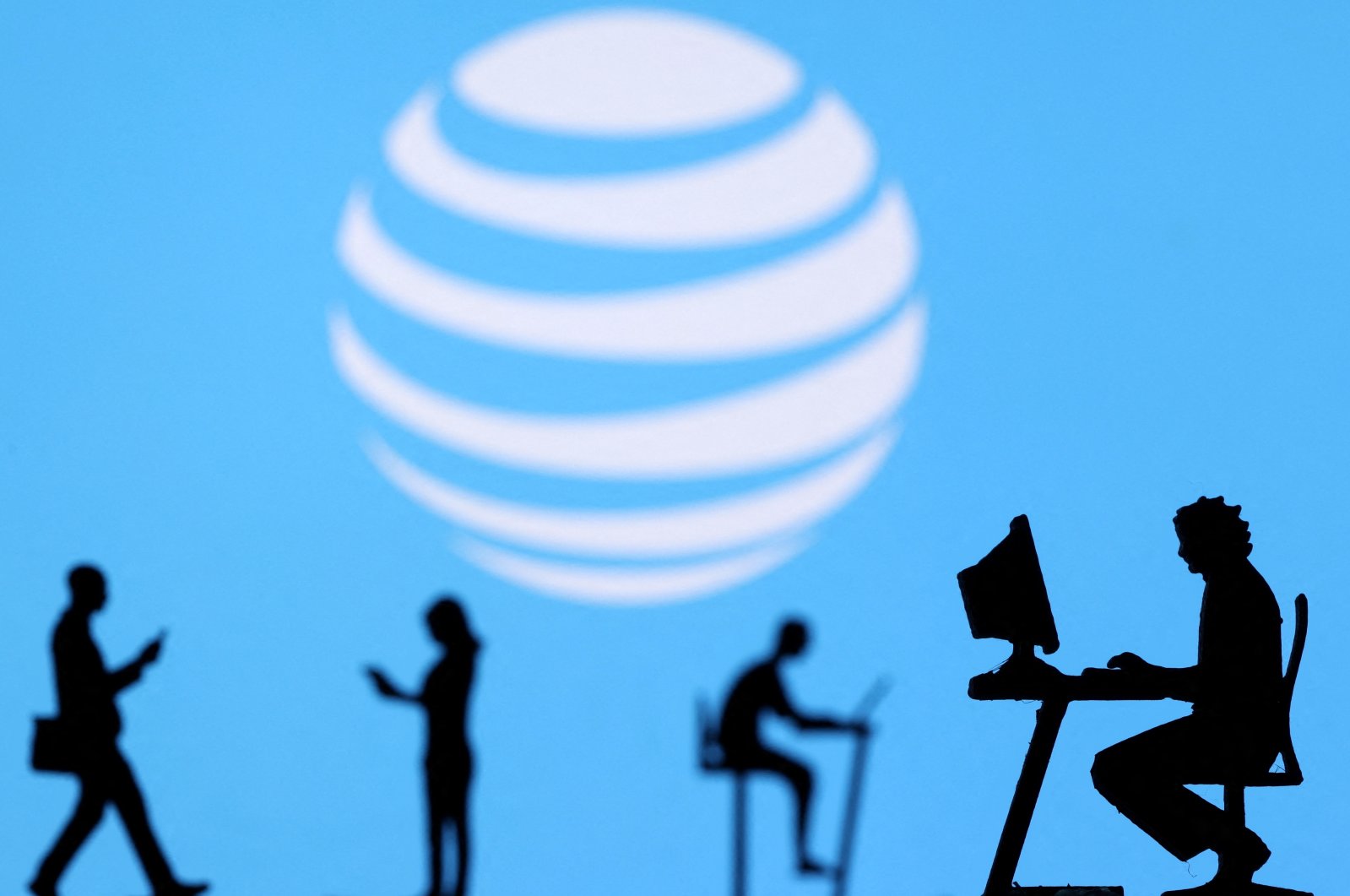 Small toy figures with laptops and smartphones are seen in front of displayed AT&T logo in this illustration, Dec. 5, 2021. (Reuters Photo)