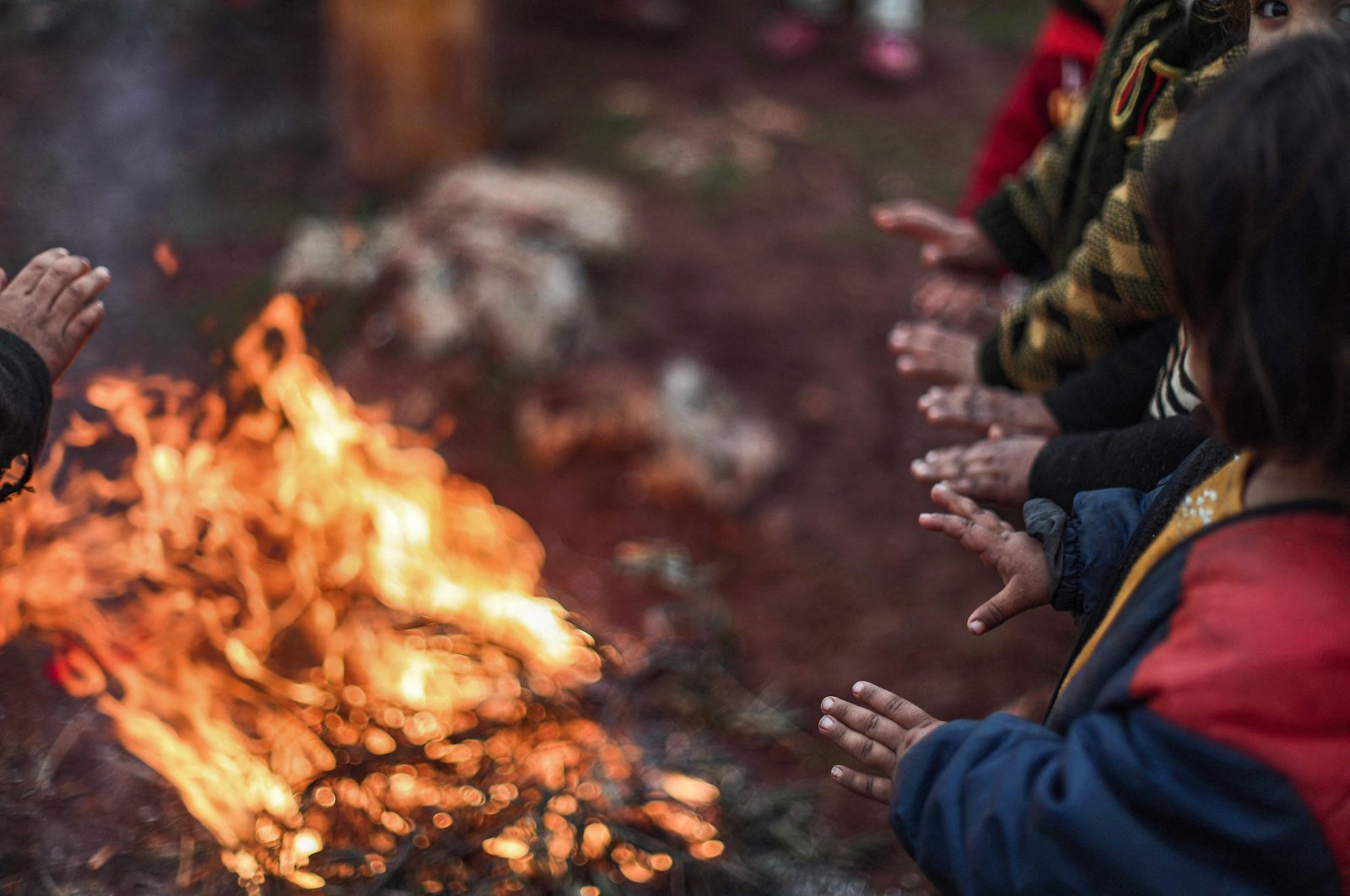Children warm up around a bonfire of burning olive branches at a make-shift camp for the displaced, near the village of Babisqa, Idlib, Syria, Dec. 17, 2021. (AFP Photo)