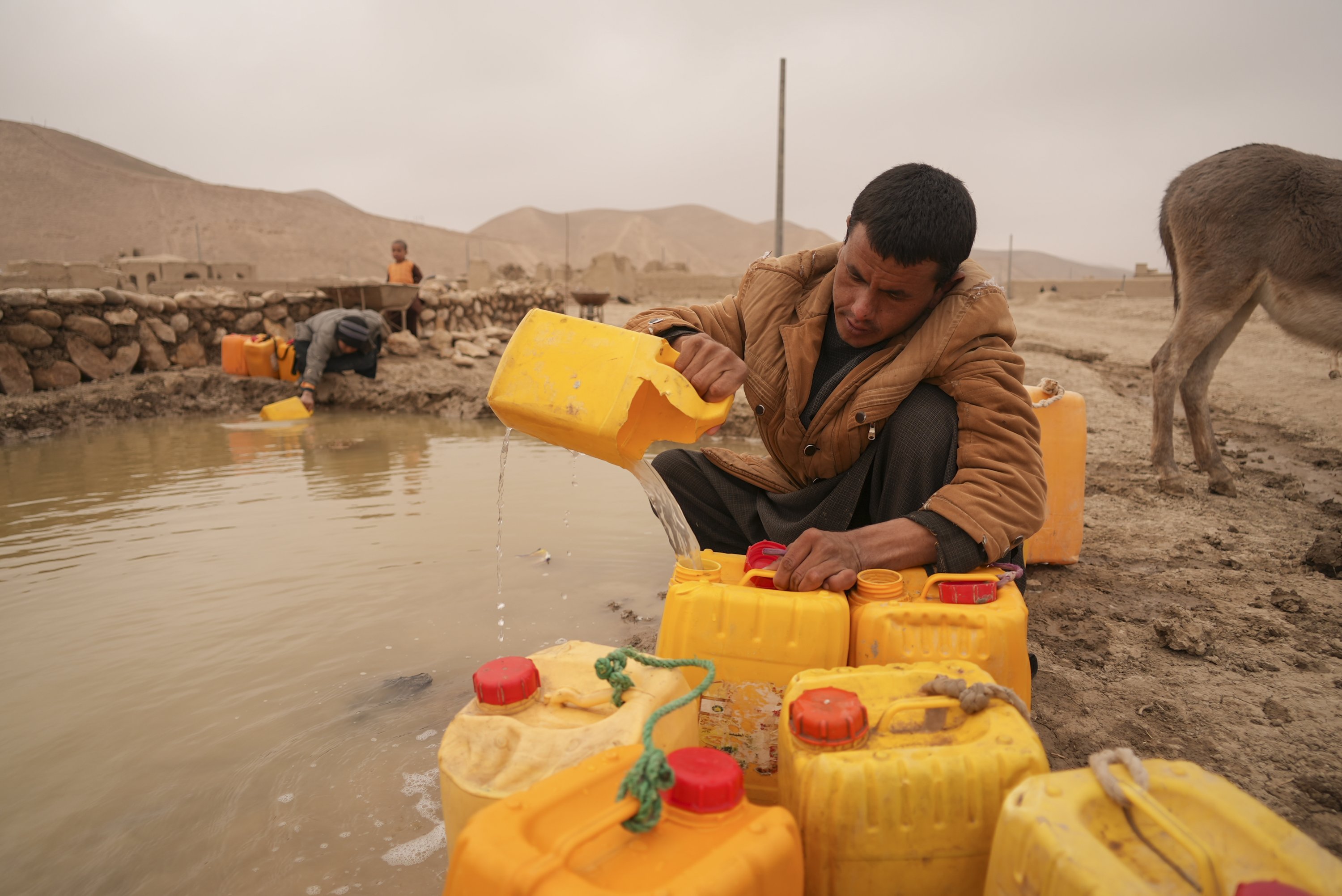 Afghan man fills oil canisters with water near the improvised dam, in Hachka, Afghanistan, Dec. 13, 2021. (AP Photo)