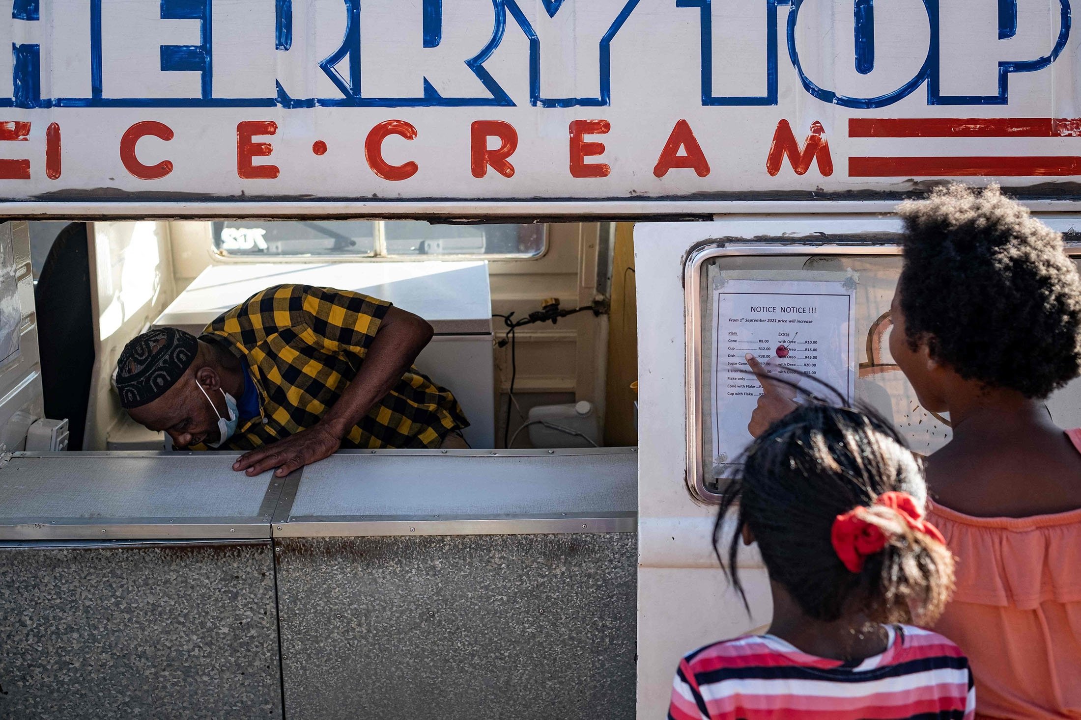 The owner of an ice cream truck, Sipho Mtshali (L), checks his stock as children look at the ice cream menu on the door of the truck in Soweto, South Africa, Nov. 19, 2021. (AFP Photo)