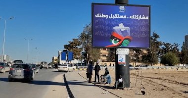 Workers sit near an electoral billboard reading in Arabic 'Our participation is the future of your country' in Tripoli, Libya, 22 December 2021. (EPA Photo)
