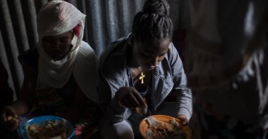Displaced Tigrayan women, one wearing an Ethiopian Orthodox Christian cross, sit in a metal shack to eat food donated by local residents at a reception center for the internally displaced in Mekele, in the Tigray region of northern Ethiopia, on May 9, 2021. (AP Photo)