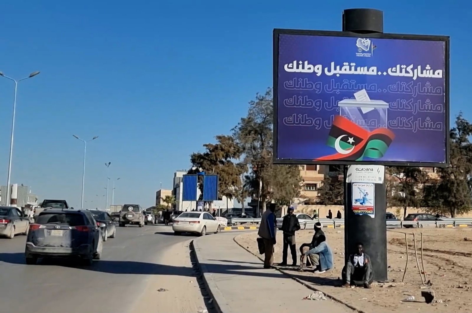 Workers sit near an electoral billboard reading in Arabic &#039;Our participation is the future of your country&#039; in Tripoli, Libya, 22 December 2021. (EPA Photo)