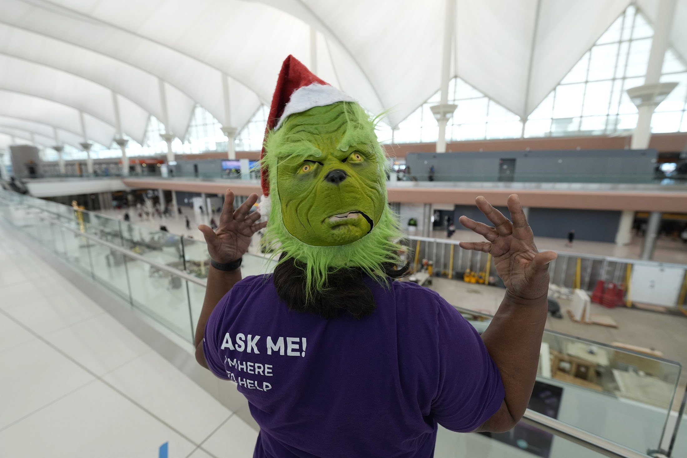 Seorang duta bandara mengenakan topeng Grinch sambil menunggu bantuan mengarahkan pemudik di terminal Bandara Internasional Denver, di Denver, Colorado, 24 Desember 2021. (AP Photo)