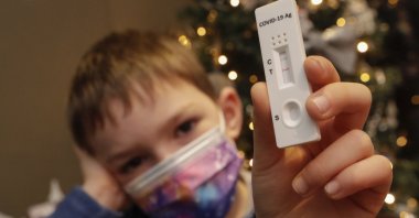 A child poses with a positive rapid COVID-19 antigen test next to a Christmas tree in Namur, Belgium, Dec. 24, 2021. (EPA Photo)