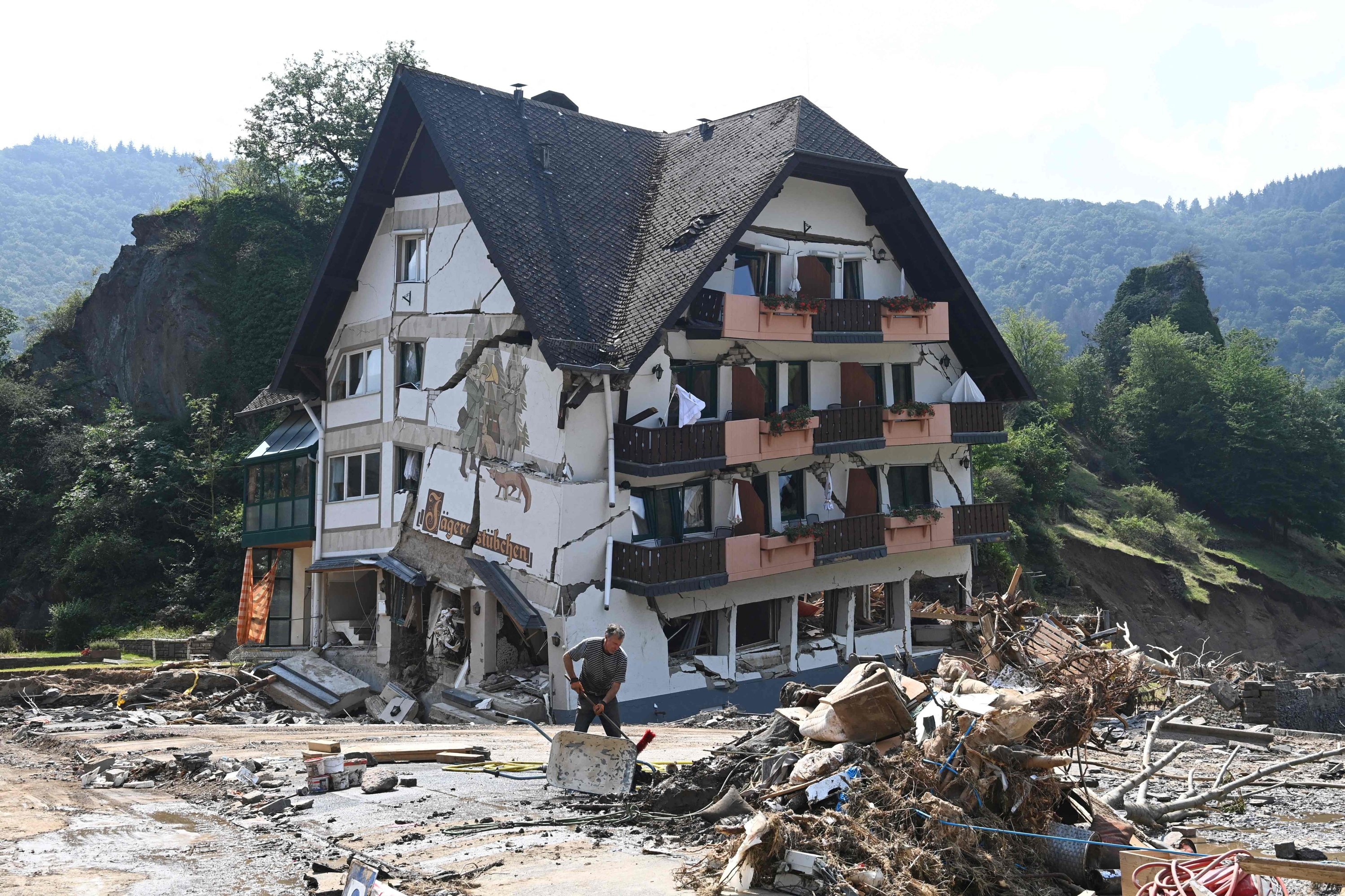 Seorang pekerja terlihat membersihkan bagian depan wisma pedesaan 'Jaegerstuebchen' yang hancur di Laach di kotamadya Mayschoss, distrik Ahrweiler, Jerman, 23 Juli 2021. (AFP Photo)