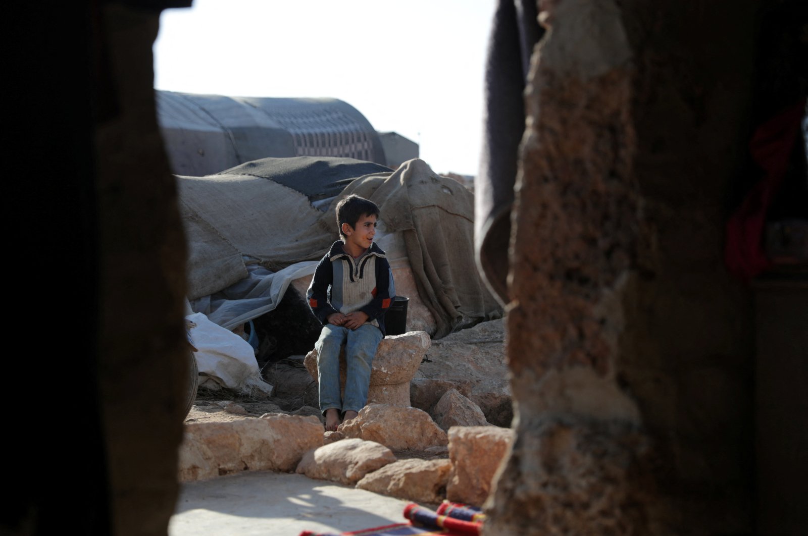 Mohammed Shiban, 7, sits on top of an ancient stone in front of the room his father Ahmad Shiban, 35, built at the UNESCO World Heritage Site of Babisqa, in the northern countryside of Idlib, Syria, Dec. 6, 2021. (REUTERS Photo)