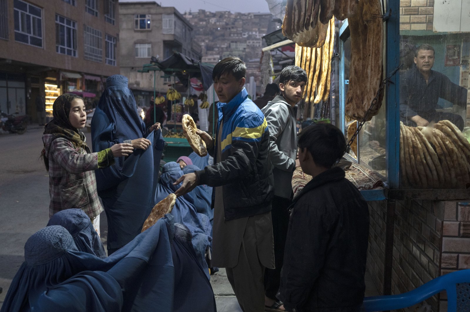 A man disributes bread to Afghan women outside a bakery in Kabul, Afghanistan, Dec, 2, 2021. (AP Photo)