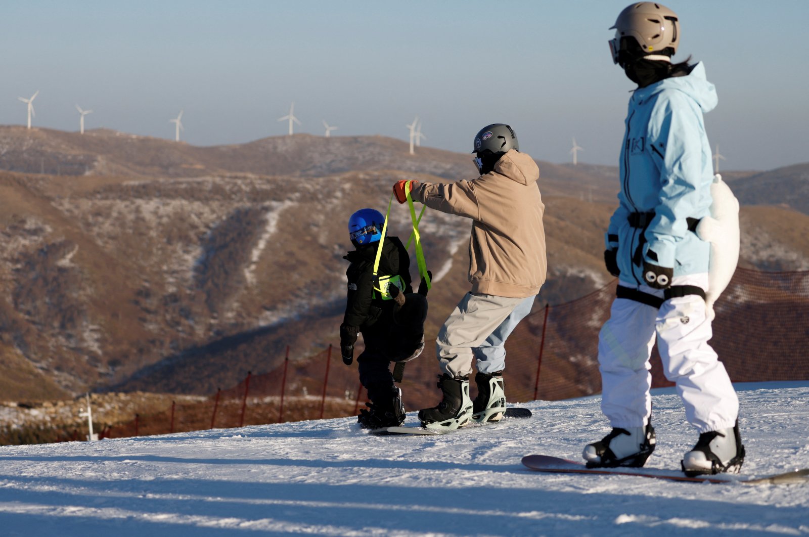 Wind turbines are seen on a slope behind visitors snowboarding at Genting Snow Park during a government-organized media tour to Beijing 2022 Winter Olympics venues, Zhangjiakou, China, Dec. 21, 2021. (Reuters Photo)