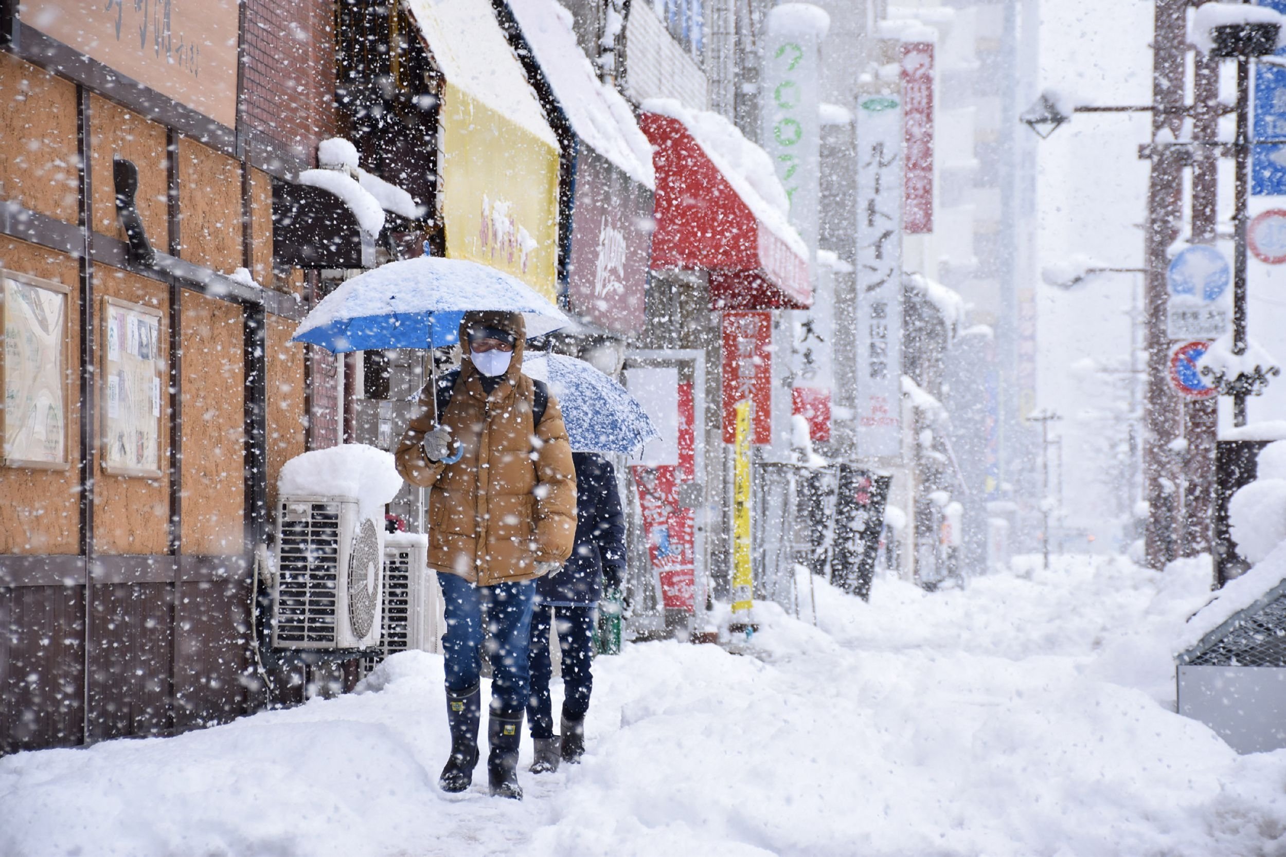 People walk along a street in heavy snow in the city of Toyama, Toyama Prefecture, brought by an extreme cold front along western and northern parts of the country, Japan, Dec. 27, 2021. (AFP Photo)