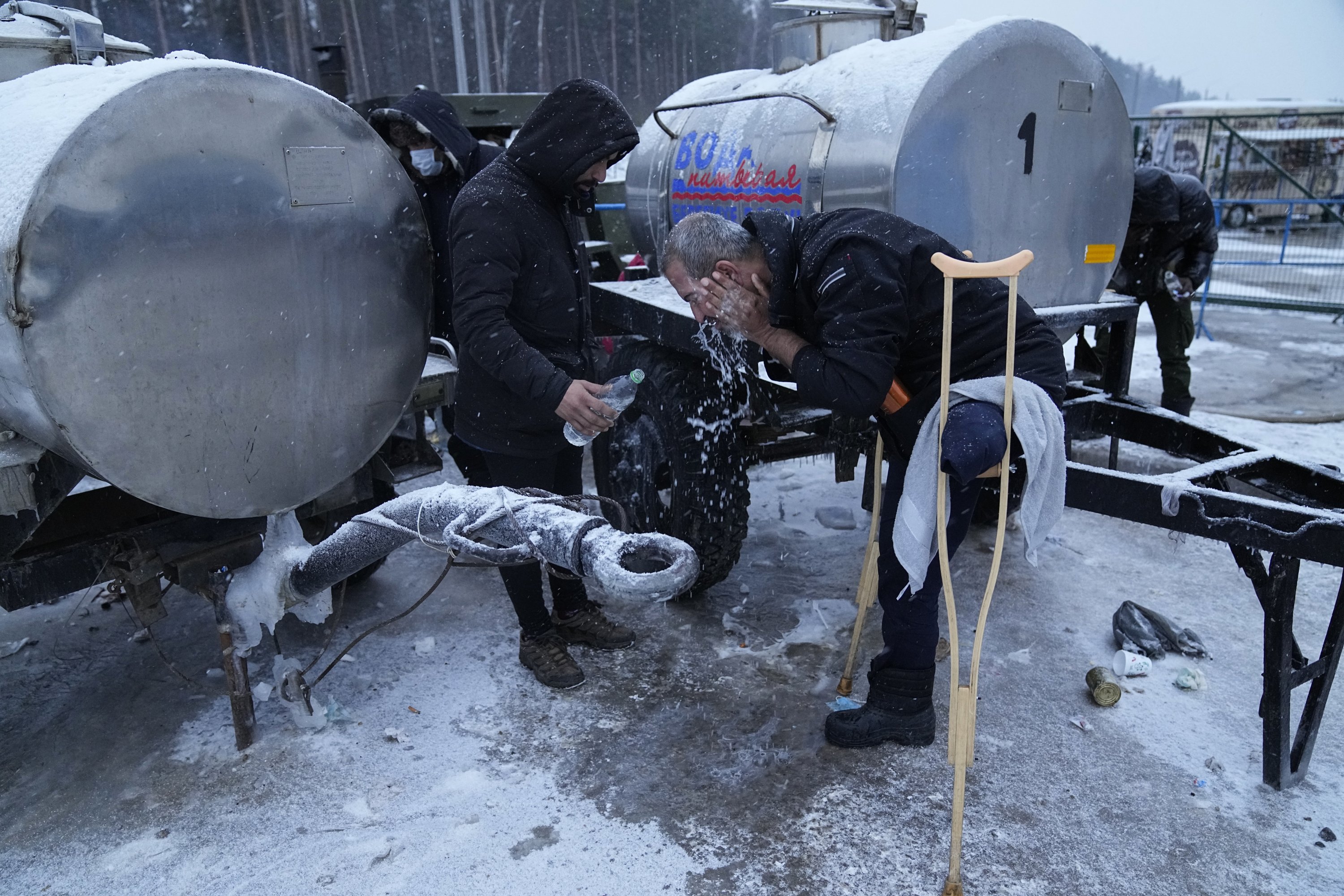 A migrant washes his head with cold water at the "Bruzgi" checkpoint logistics center at the Belarus-Poland border near Grodno, Belarus, Dec. 23, 2021. (AP Photo)