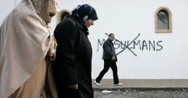 Muslim residents walk past racial slurs painted on the walls of a mosque in the town of Saint-Etienne, central France, Feb. 8, 2010. (AP Photo)