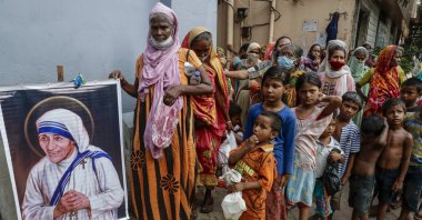 Homeless people gather beside a portrait of St. Teresa, the founder of the Missionaries of Charity, to collect free food outside the order's headquarters in Kolkata, India, Aug. 26, 2021. (AP Photo)