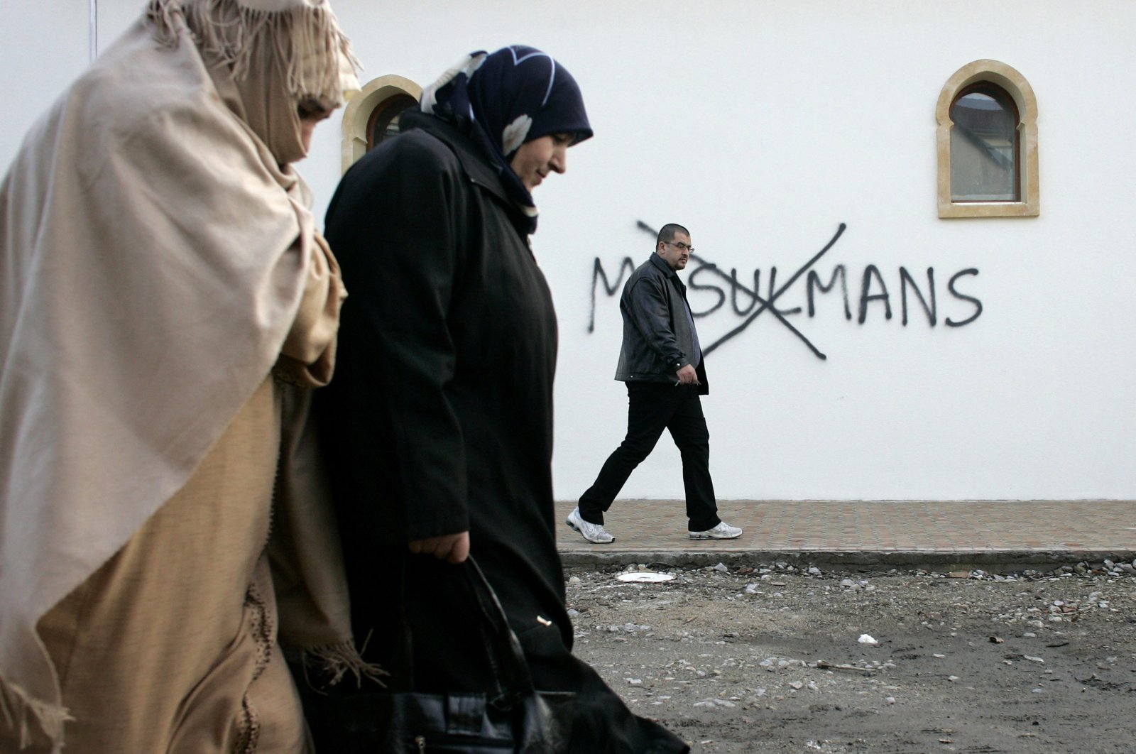 Muslim residents walk past racial slurs painted on the walls of a mosque in the town of Saint-Etienne, central France, Feb. 8, 2010. (AP Photo)