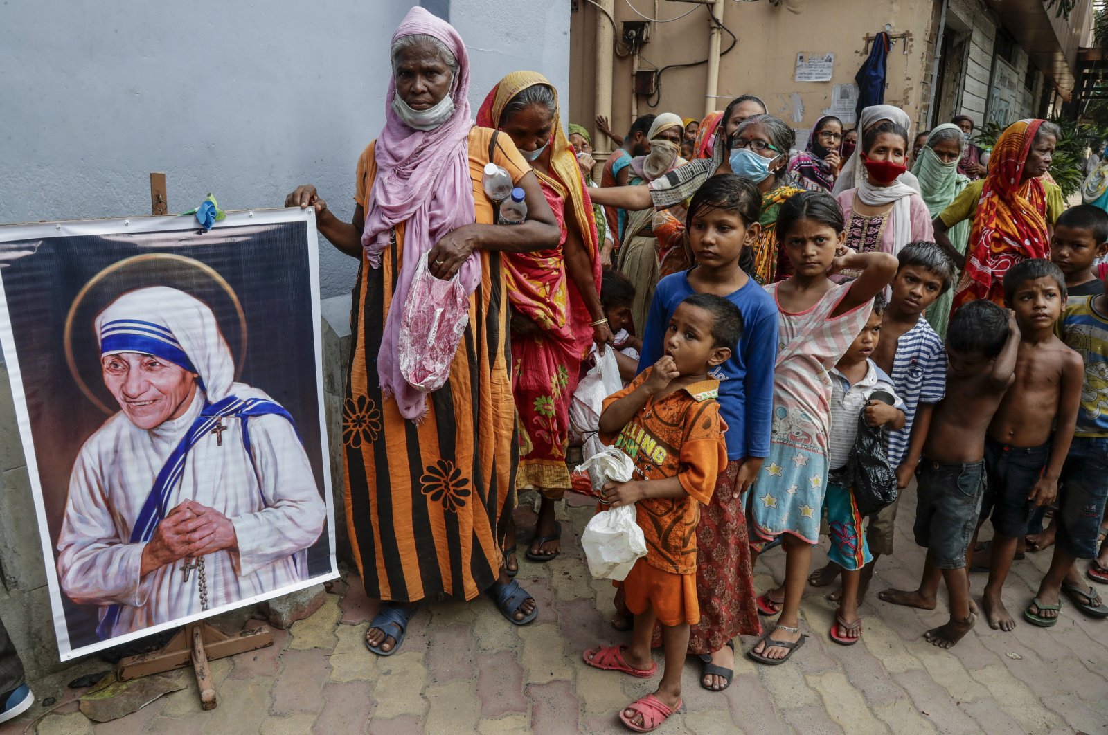Homeless people gather beside a portrait of St. Teresa, the founder of the Missionaries of Charity, to collect free food outside the order&#039;s headquarters in Kolkata, India, Aug. 26, 2021. (AP Photo)