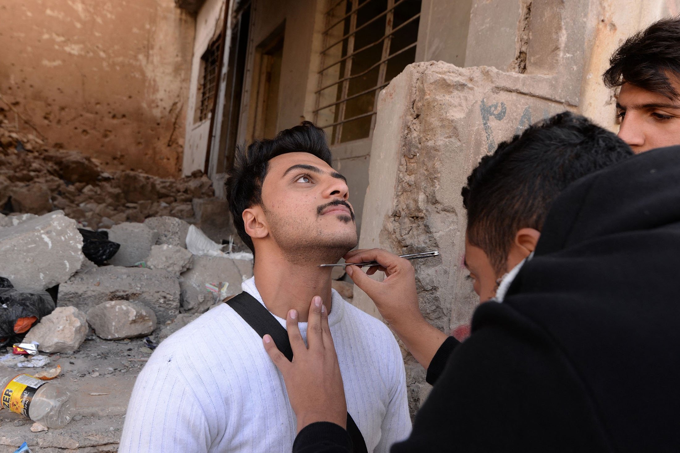 Penata rias dari sekolah film mempersiapkan seorang aktor sebelum syuting adegan di kota utara Mosul yang dilanda perang, Irak, 15 Desember 2021. (AFP Photo)