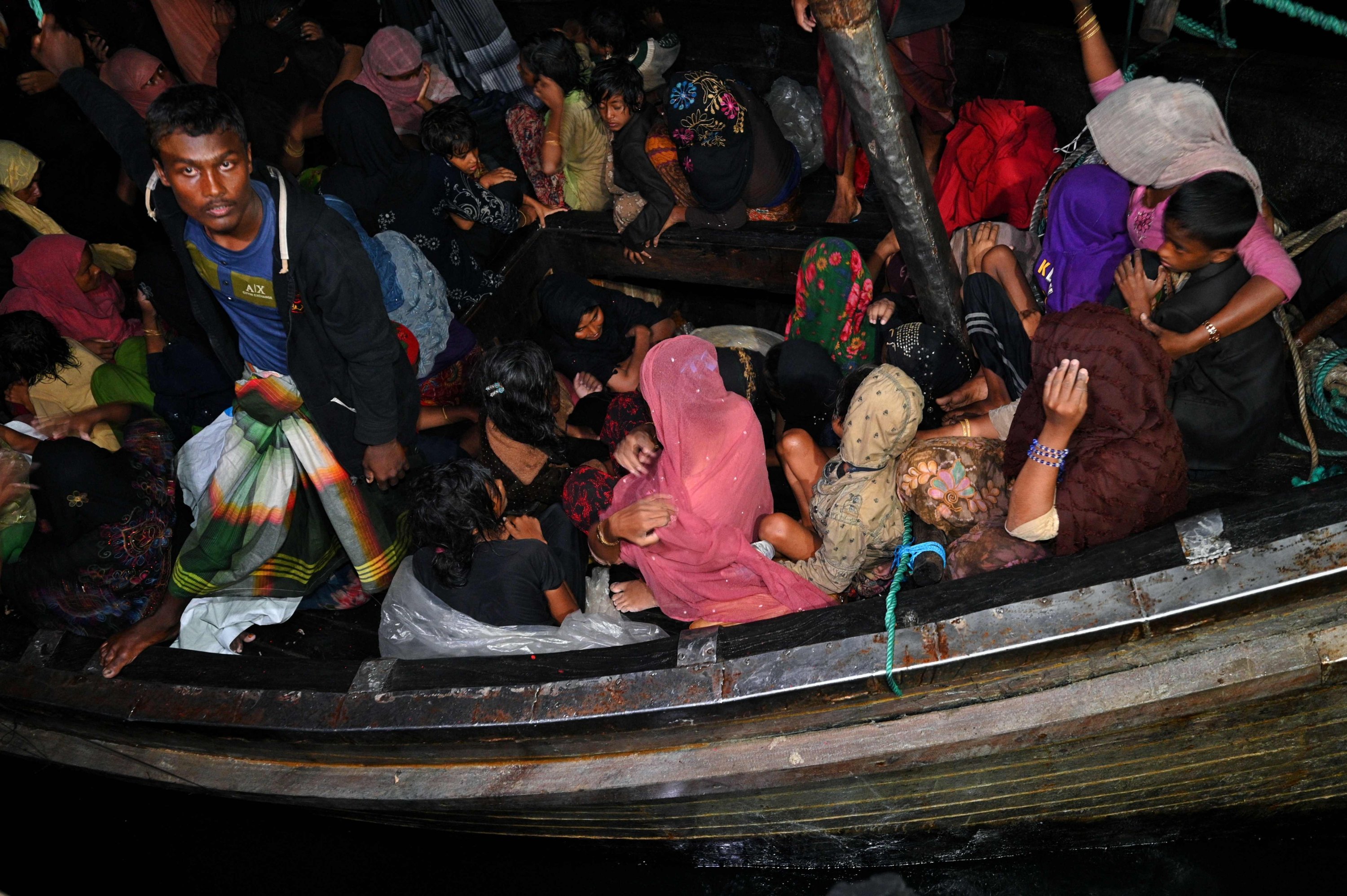 Pengungsi Rohingya duduk di atas perahu kayu setelah mereka diselamatkan oleh angkatan laut Indonesia di perairan Bireuen, setibanya mereka di pelabuhan Krueng Geukueh di Lhokseumawe, di pantai utara provinsi Aceh, Indonesia, 31 Desember 2021. (AFP Photo)