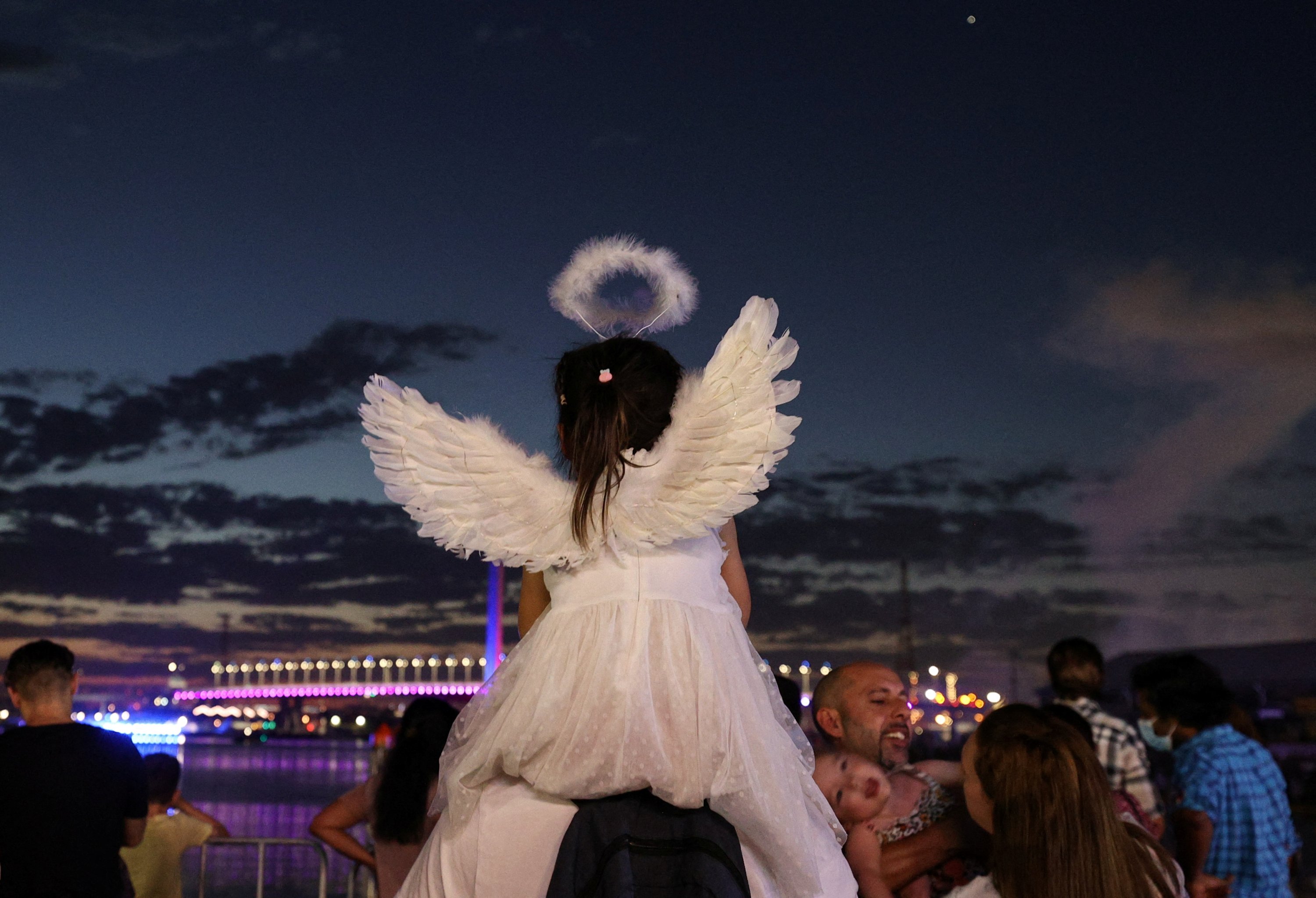Seorang anak mengenakan sayap malaikat saat keluarga merayakan Malam Tahun Baru di tepi Sungai Yarra, saat varian omicron dari virus corona terus menyebar di Melbourne, Australia, 31 Desember 2021. (Foto Reuters)