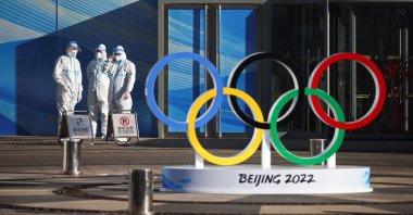 Workers in PPE stand next to the Olympic rings inside the closed-loop area near the Bird's Nest in Beijing, China, Dec. 30, 2021. (Reuters Photo)