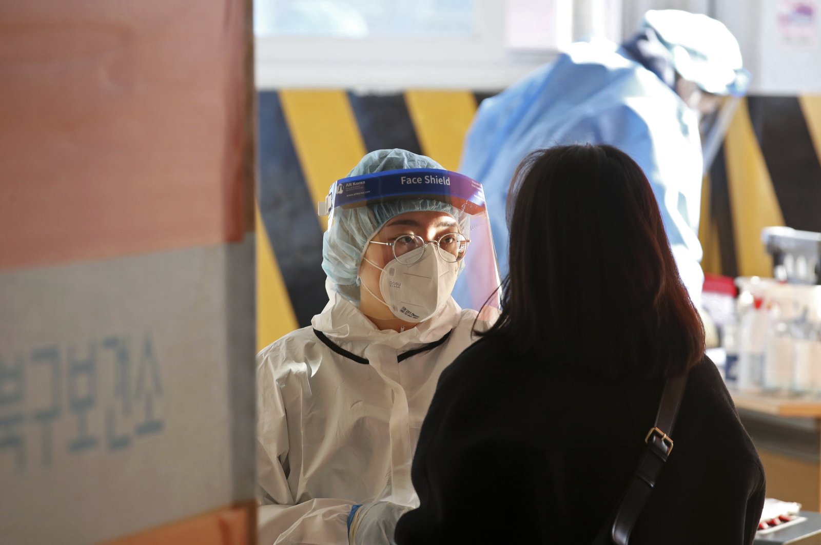A medical worker wearing protective gear takes a sample from a woman at a temporary screening clinic for the coronavirus in Gwangju, South Korea, Jan. 3, 2022. (AP Photo)