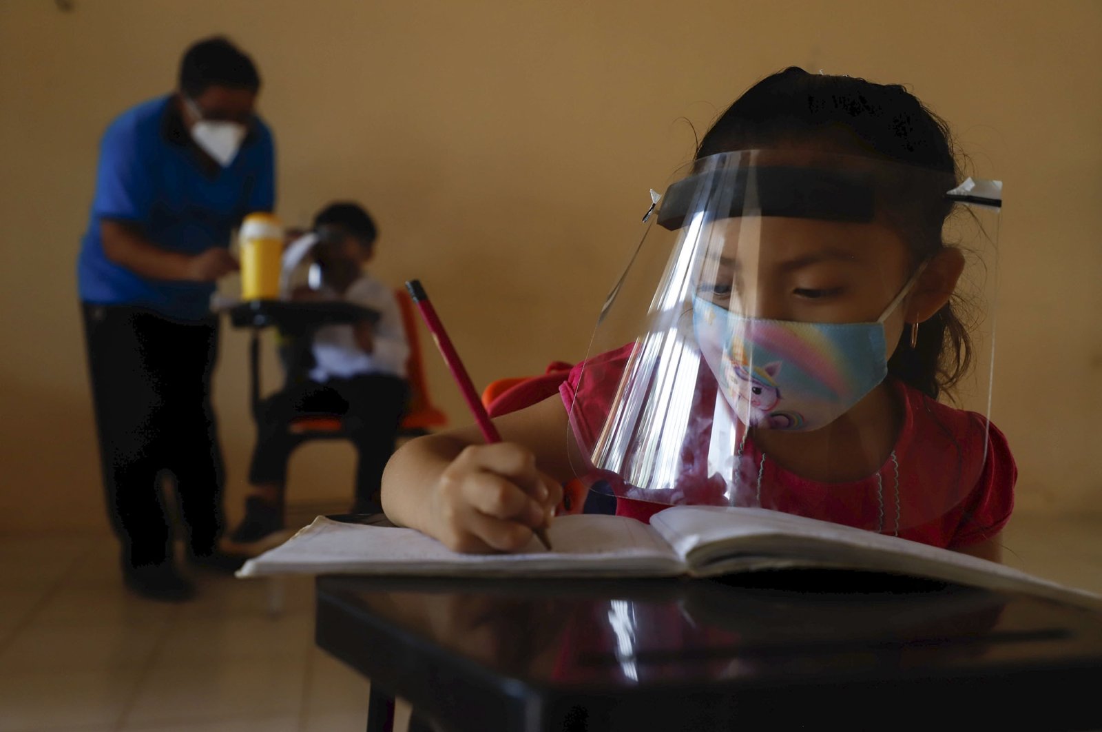 A 10-year-old girl wearing a mask and a face shield writes in her notebook during the first day of class at the Valentin Gomez Farias Indigenous Primary School in Montebello, Hecelchakan, Campeche state, Mexico, April 19, 2021. (AP Photo)