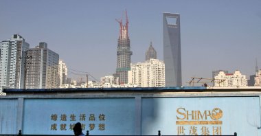 A man walks past a wall carrying the logo of Shimao Group, with residential buildings and the financial district of Pudong seen in the background in Shanghai, China, Jan. 1, 2013. (Reuters Photo)